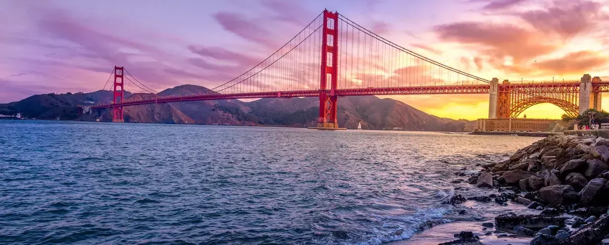 A Ponte Golden Gate ao pôr do sol com um céu multicolorido e a Baía 来自贝博体彩app em primeiro plano.